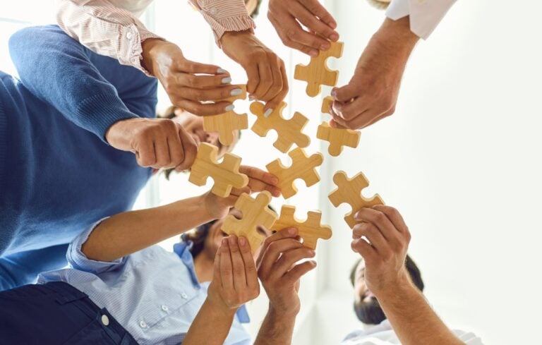 Happy company employees joining parts of jigsaw puzzle during work meeting or team building activity